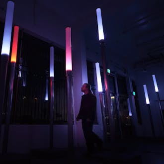 Cory Barr stands in a darkened room, looking at colorful illuminated columns.