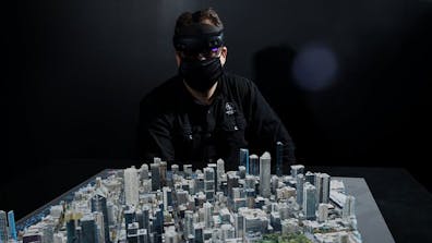 Man wearing a mask and VR headset standing over a digital 3D model of a city