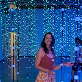 Sarah Koon stands in a room with strands of spherical lights, smiling.