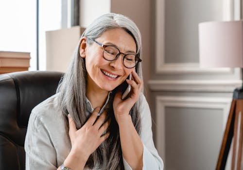 A woman with glasses is talking on the phone, appearing cheerful and engaged in the conversation.