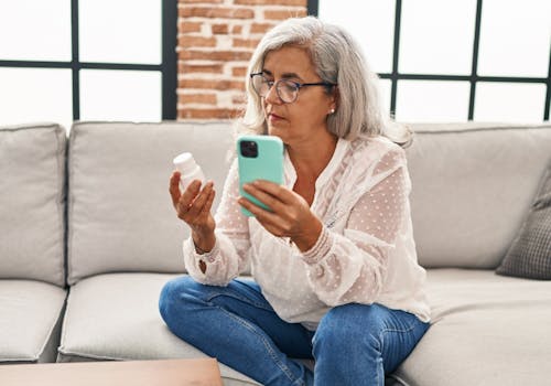 A female member sitting on couch reviewing her prescription with her mobile phone.