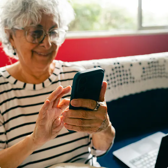 An older woman wearing glasses and a striped shirt using a smartphone while sitting on a couch.