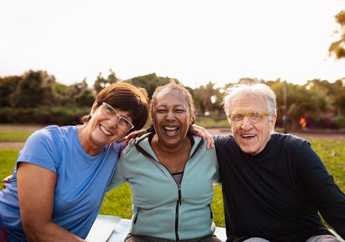 Three older adults relax on a blanket in the park, enjoying the sunny day and each other's company.