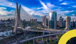 Imagem panorâmica da cidade de São Paulo em um dia ensolarado com céu azul. A foto tem como foco a Ponte Estaiada e os prédios da cidade.