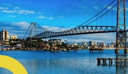 Imagem da ponte principal de Florianópolis, em Santa Catarina. A foto mostra a ponte cercada pela cidade em um dia ensolarado com céu azul.