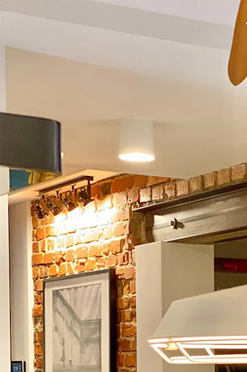 White industrial lamp above kitchen countertop, red brick on wall in hallway, large dream catcher on wall