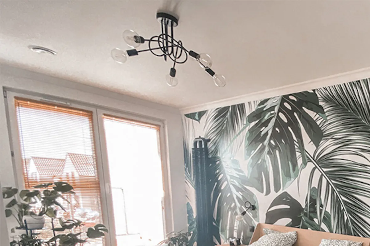 intérieur de la chambre avec lit en bois clair, papier peint décoratif à motif floral et chaise ajourée noire