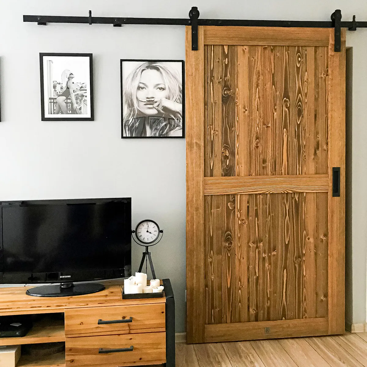 sliding doors in a small apartment, wooden door installed on black sliding system, black and white posters on the wall, steel and wood TV cabinet, black decorative standing clock