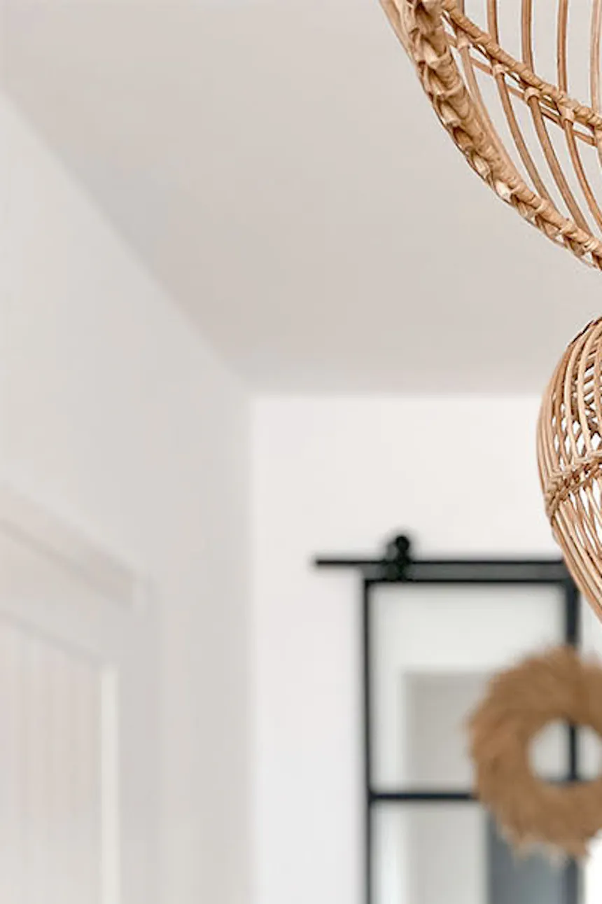 Glass vase on a wooden tray and woven pendant lamps in a white-walled living room