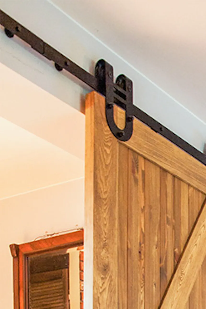 rustic wooden door, brushed wood sliding door, barn door, sliding door with a horseshoe system, blue sofa in the living room, brick on the wall