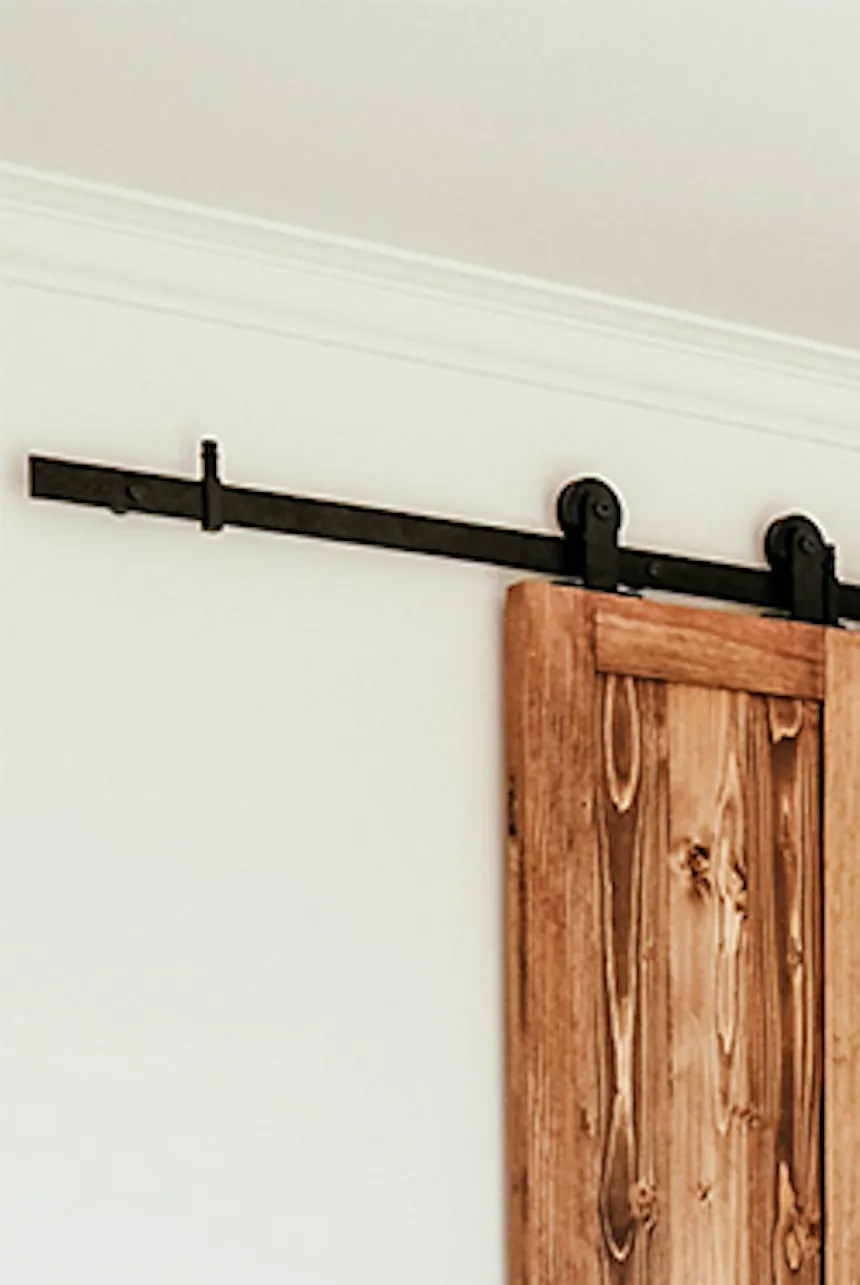 couvre-lit beige et oreillers décoratifs dans la chambre avec une petite armoire cachée derrière des portes coulissantes