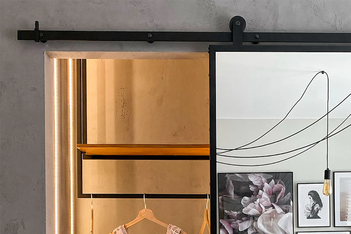 Sliding doors in a black metal frame closing a small loft-style walk-in closet