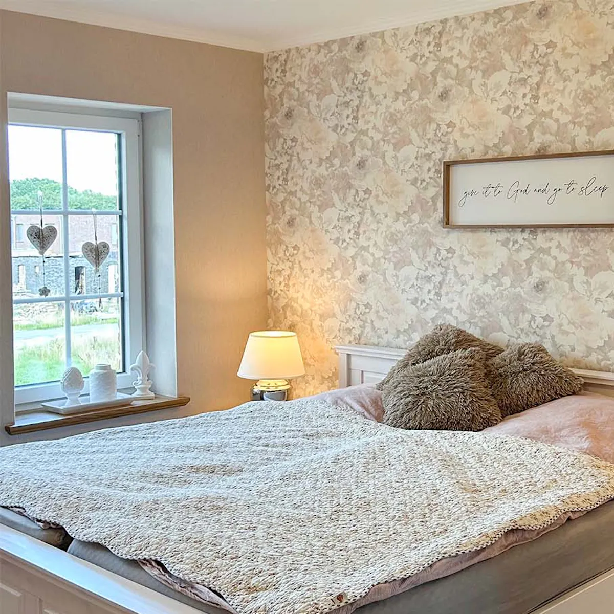 un grand lit contre un mur avec du papier peint à fleurs dans une chambre décorée dans un style farmhouse moderne