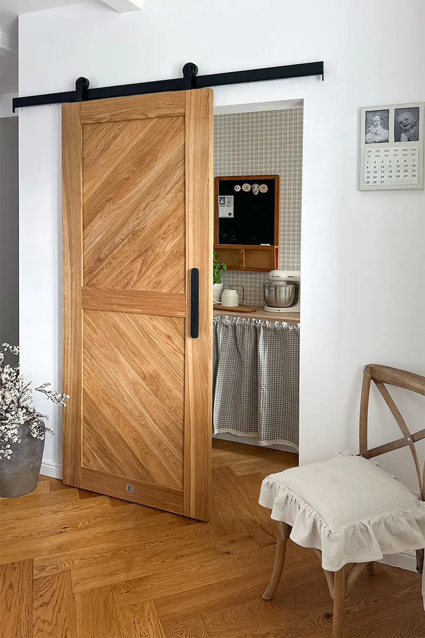 An ajar oak sliding door with a diagonal board pattern, leading to the pantry next to the kitchen.