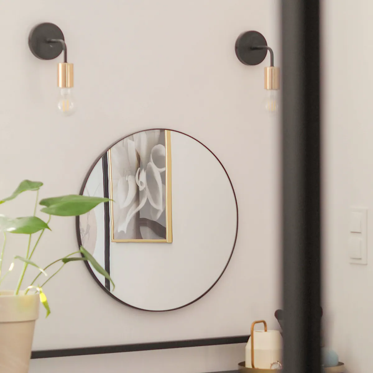un miroir rond sur un mur blanc est suspendu au-dessus d'un bureau noir et d'une chaise en rotin