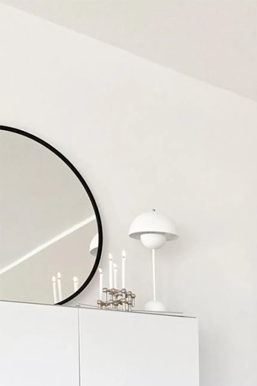 Round light wood table in Nordic style, white flowers in white vase on side table, white dresser, beige sofa