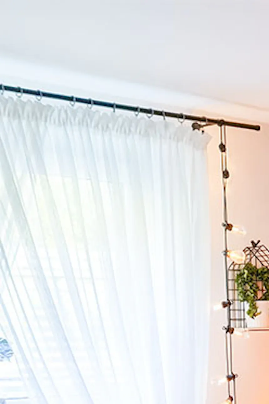 braided decorative plaid on a white bed, decorative pillows for a bed in a bedroom, Scandinavian interior, black lamps hanging above the bed, floral decorations on the wall in the bedroom