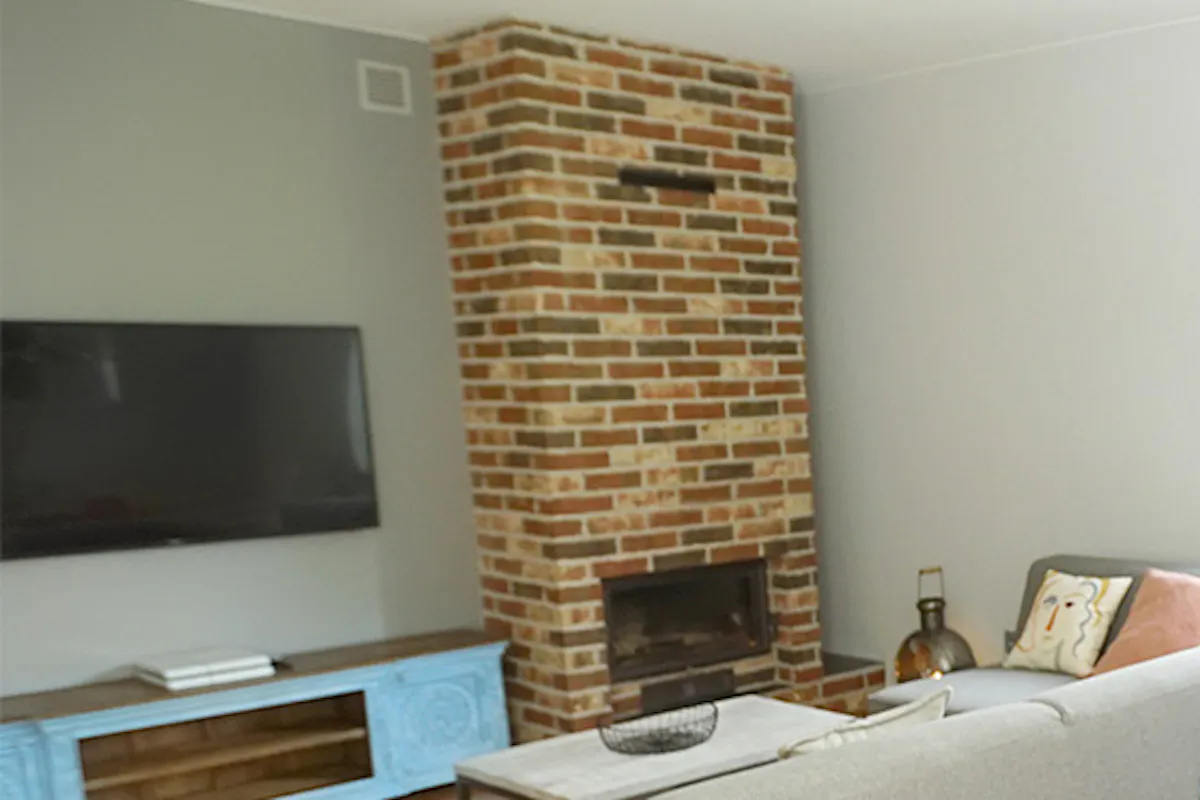 Living room arrangement with masonry fireplace, gray sofa, colorful accessories, and dining nook
