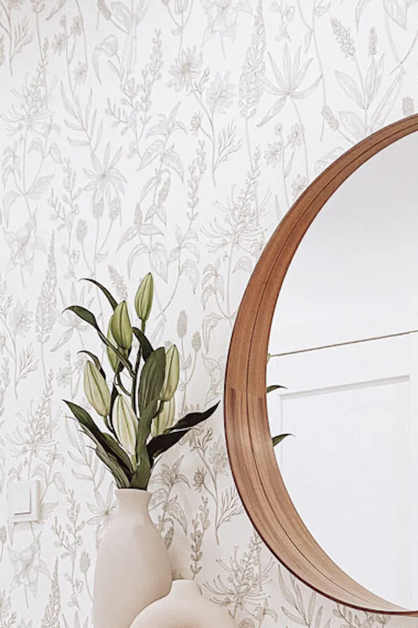white narrow chest of drawers in the hall, round mirror in a wooden frame, monochrome wallpaper with floral patterns