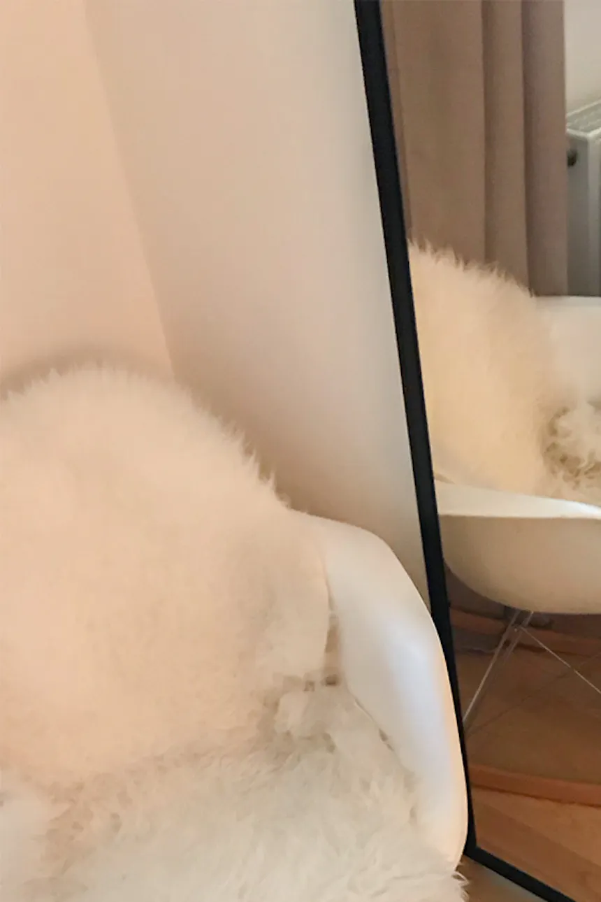Large mirror in metal frame next to white armchair