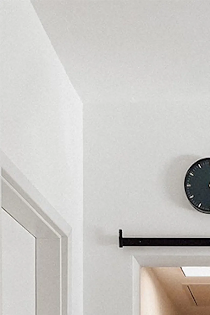 Glass sliding door separating hallway, light marble flooring, white walls with black accessories and clock, metal glass door.