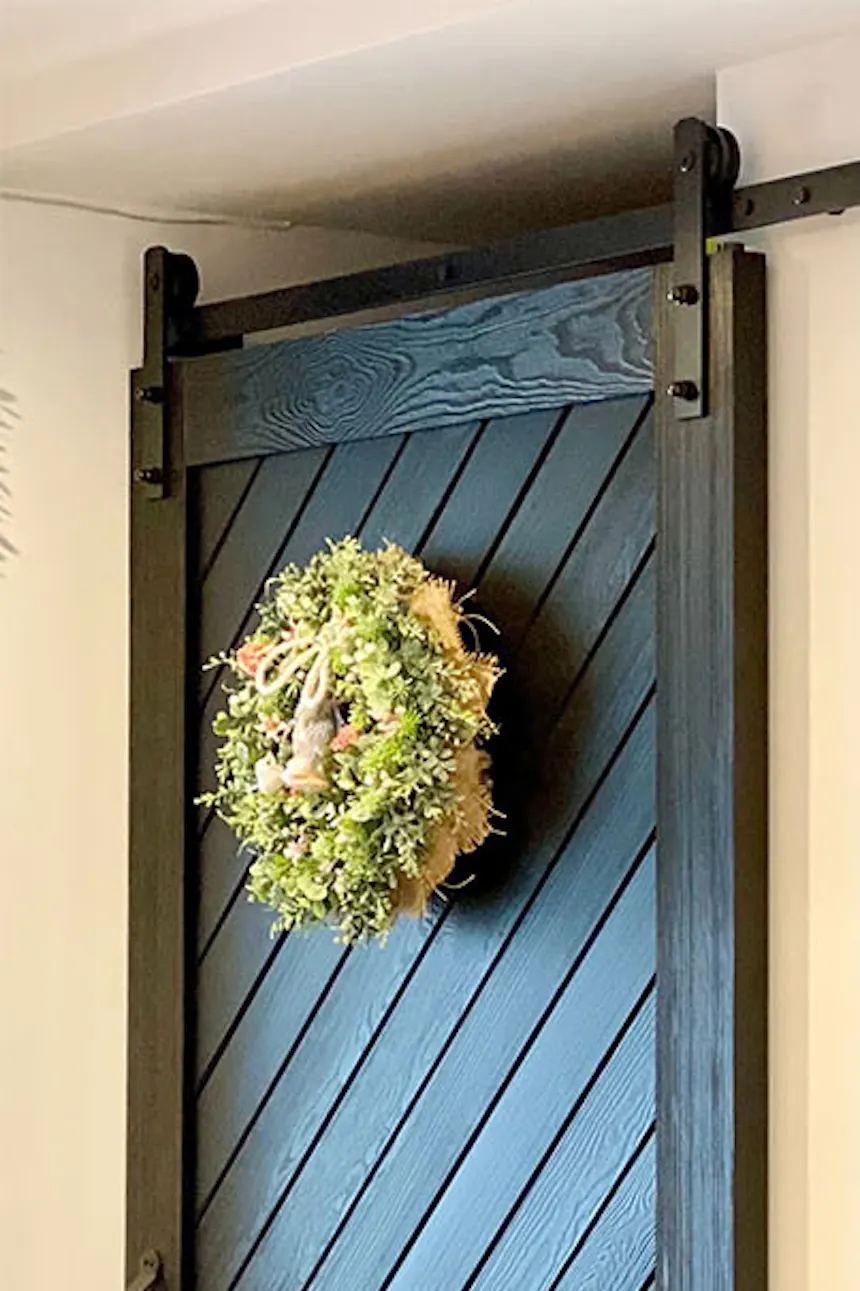 Sliding door for pantry, black solid wood sliding door, decorative wreath on door, red brick on wall, decorative paintings on white wall