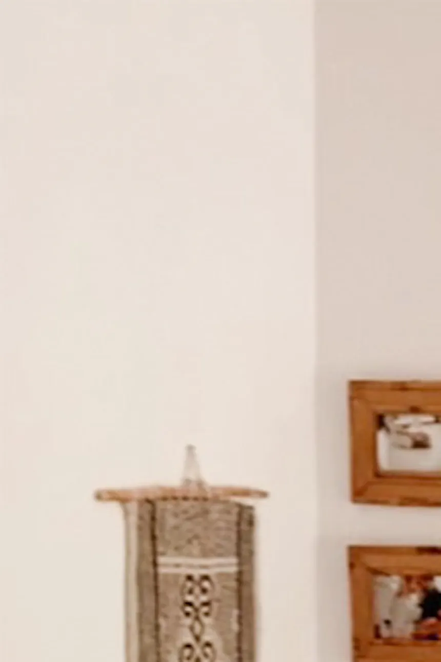 white walls in a natural bedroom, boho decorations on a white wall in the bedroom, a bed with a black frame, woven poufs, pictures in wooden frames on a white wall