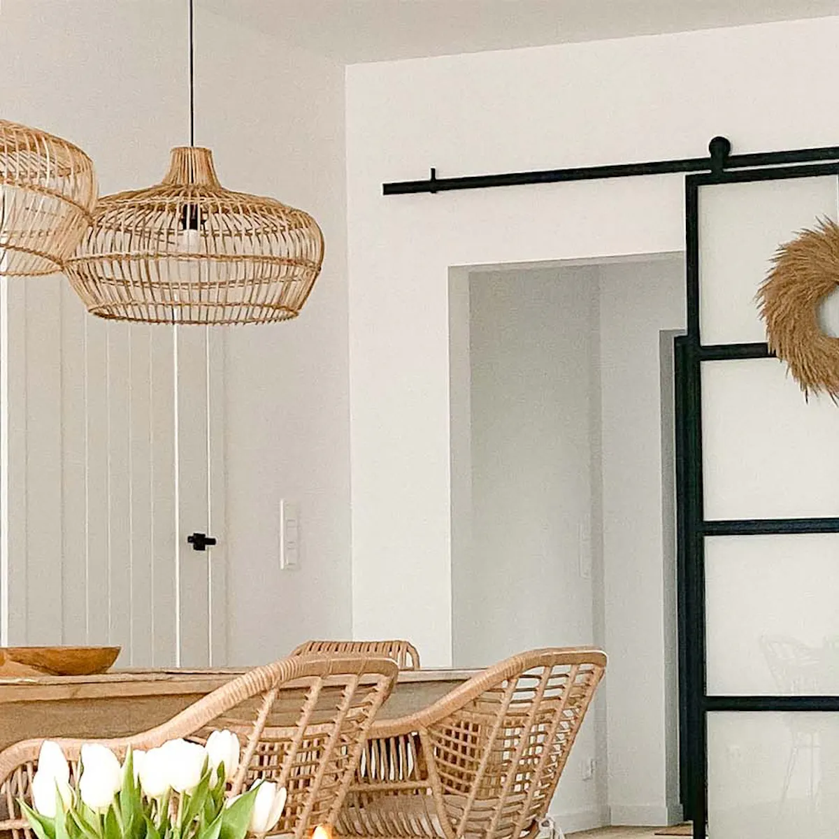 Rattan chairs on metal legs, large wood table, woven pendant lamps, and glass sliding doors with metal frames