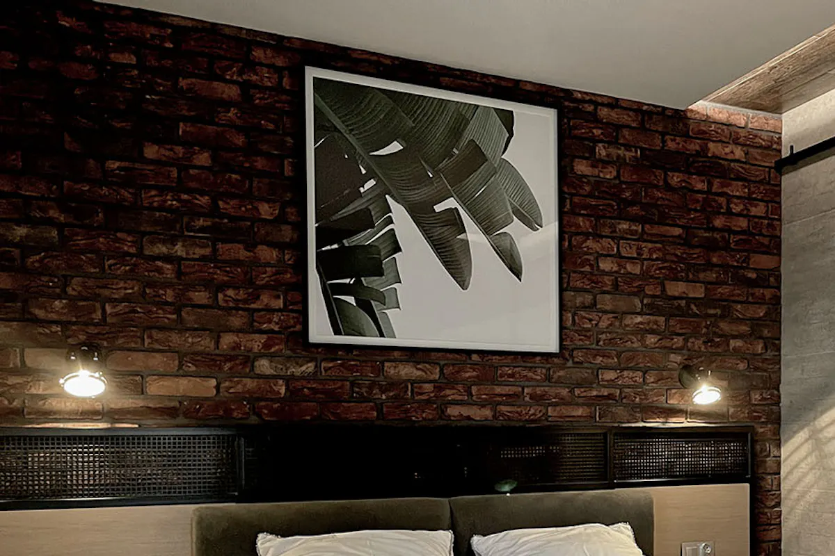 Industrial bedroom with red brick wall, black and white poster above bed, and sliding door to bathroom
