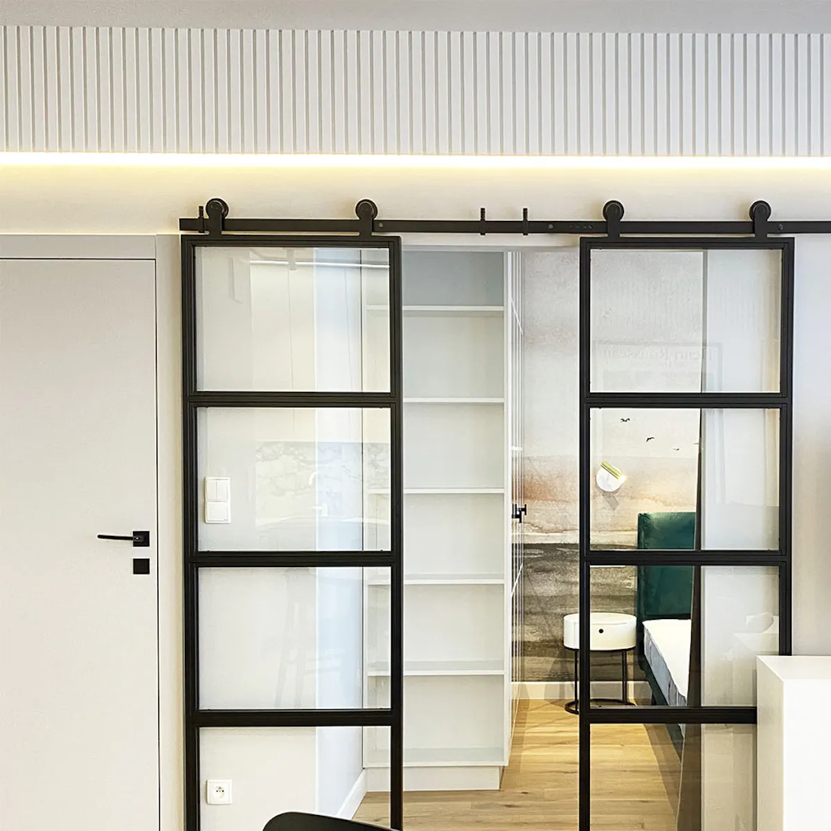 Double glass sliding doors in metal frame separating living and bedroom, white walls and light flooring in modern apartment