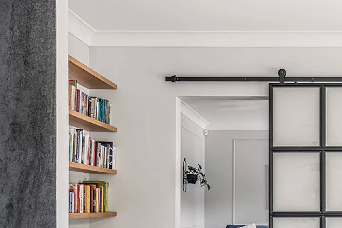 Reading corner with blue denim sofa, metal and glass sliding doors, doorway between rooms, hardwood floor in living room, bright room, light wood furniture, blue and yellow decorative pillows, wall planter