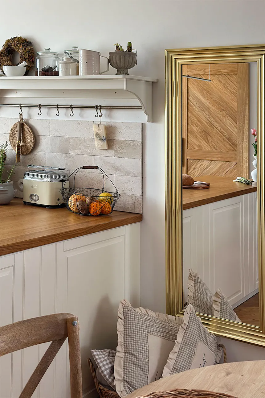 Un miroir dans un cadre doré reflétant les portes coulissantes en chêne CARO et une partie de la cuisine claire.