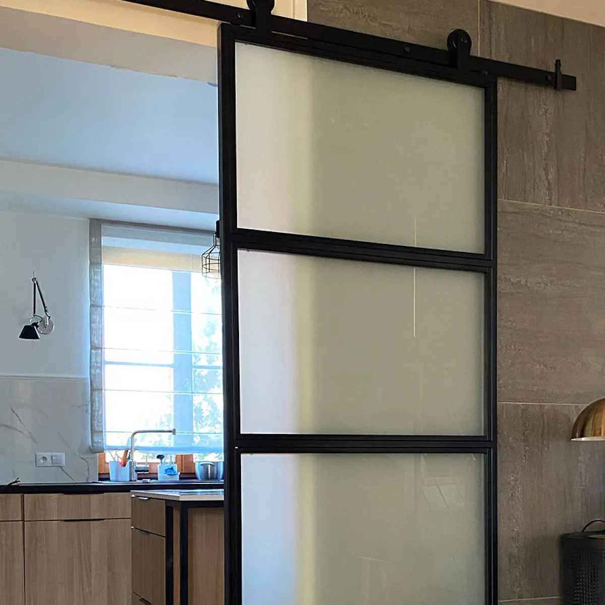 Loft glass doors, metal glass door for kitchen, bright kitchen with island, graphite tiles on wall, golden lamp on black console, black decorative console with mirror in hallway