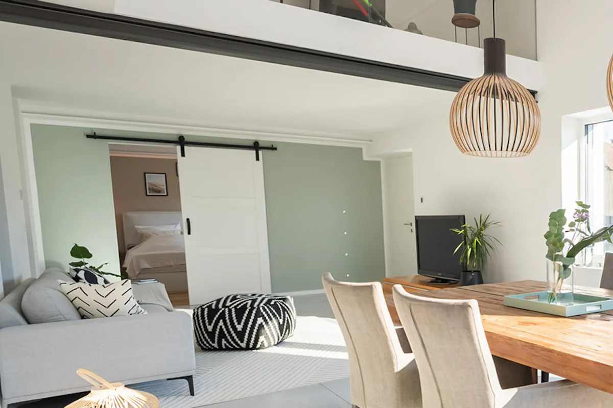 Modern spacious living room with solid dining table, beige upholstered chairs, gray sofa, white sliding doors
