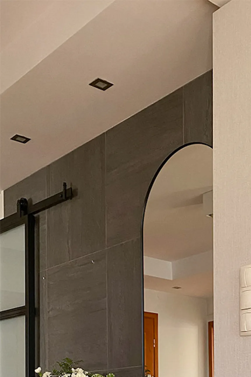 Cream and gray tones in passageway between living room and entryway, black decorative console in entryway, mirror above console, wicker basket