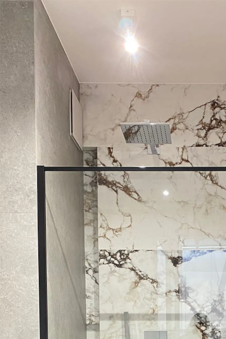 Minimalist shower enclosures in modern bathroom, stone-patterned tiles, white bathroom fixtures