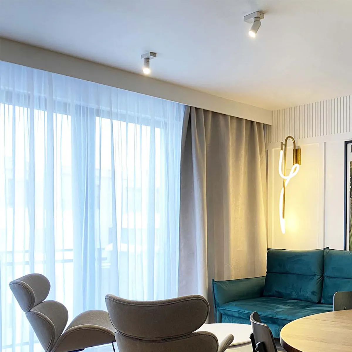 Emerald green sofa, gray armchairs on metal frame, living and dining area combined in modern apartment, round dining table, modern lighting, white walls and gray accessories