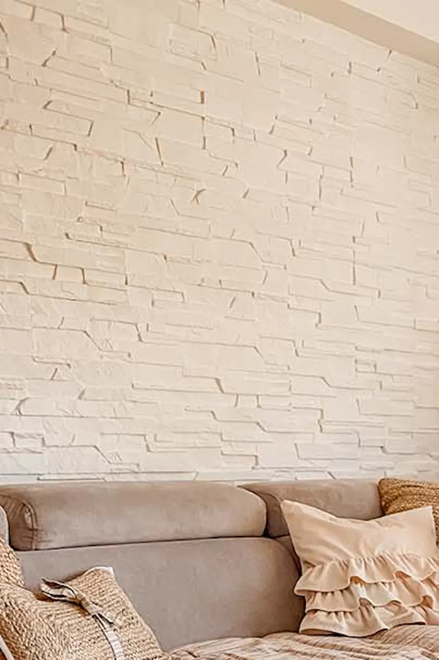 un mur de briques blanches, un grand canapé gris et une table palette dans le salon