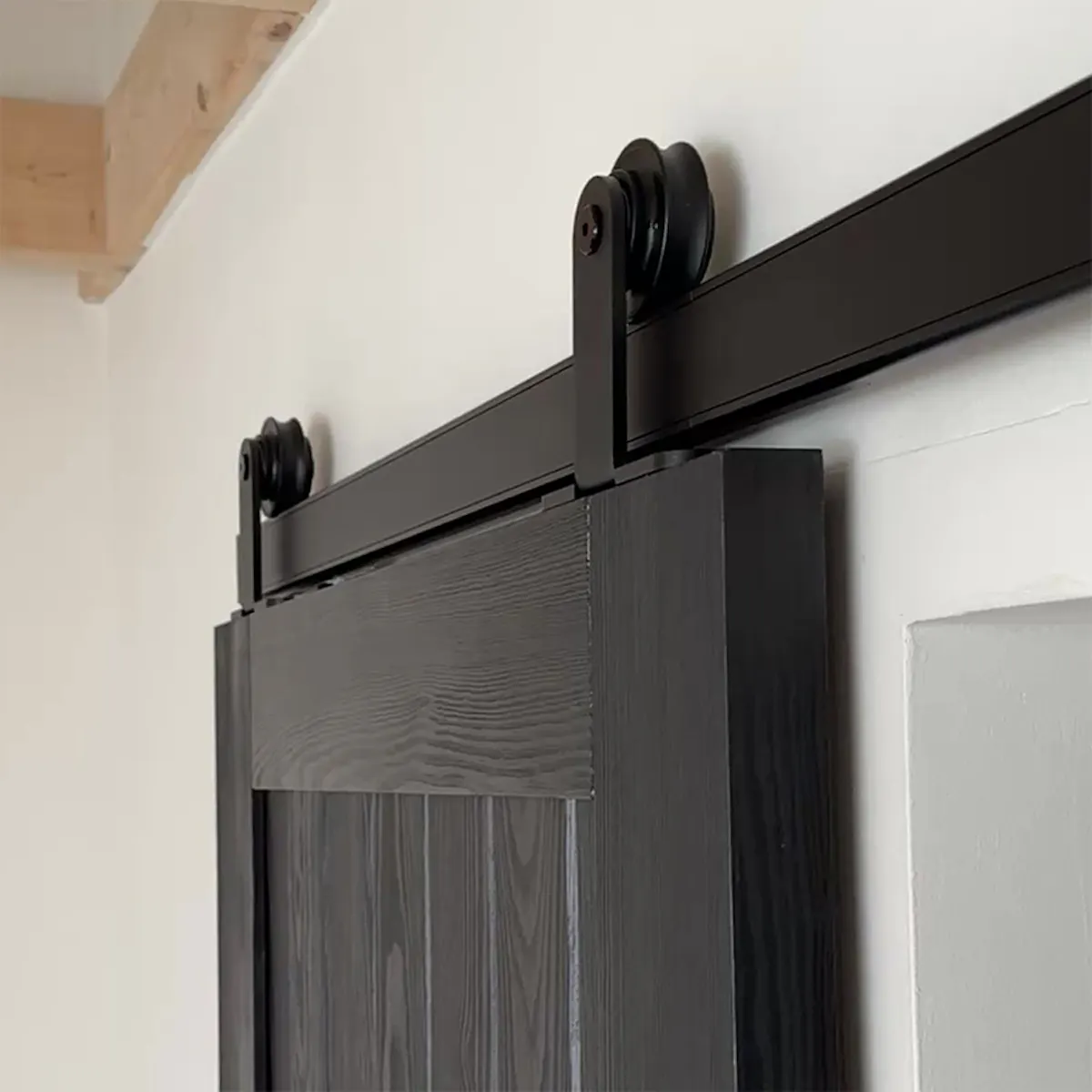 Gros plan sur un système coulissant noir installé sur une porte en bois noire.