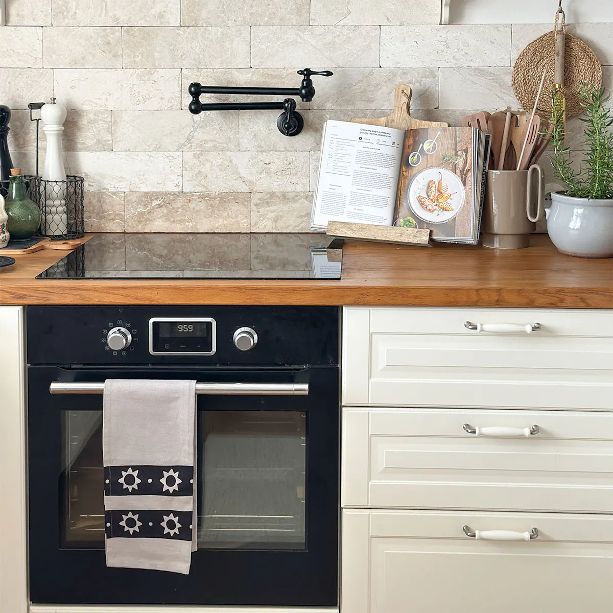 Des meubles de cuisine clairs avec un plan de travail en chêne, une plaque de cuisson noire et un robinet mural de remplissage de marmite (Pot Filler).