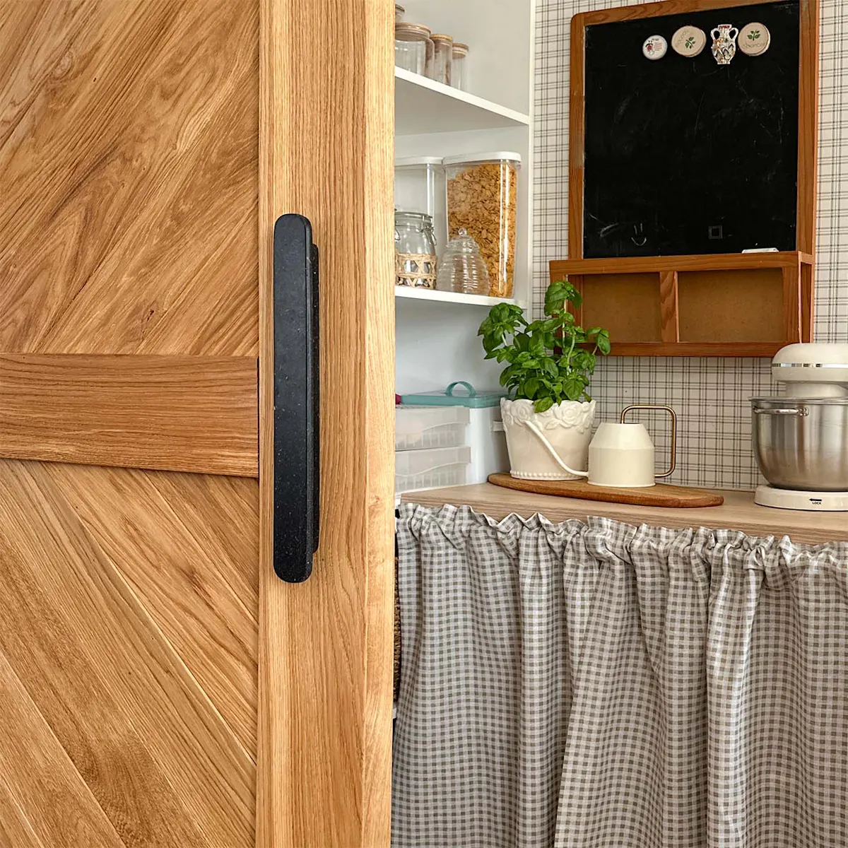 A close-up of a matt black handle on an oak sliding door, set against the backdrop of a well-organised pantry.