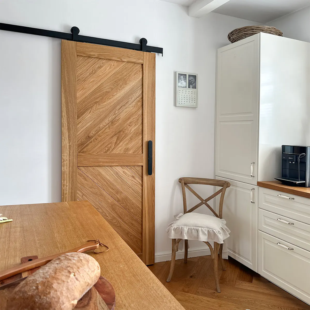 Closed CARO oak sliding door in a bright kitchen beside cream fitted cabinetry and a wooden chair.