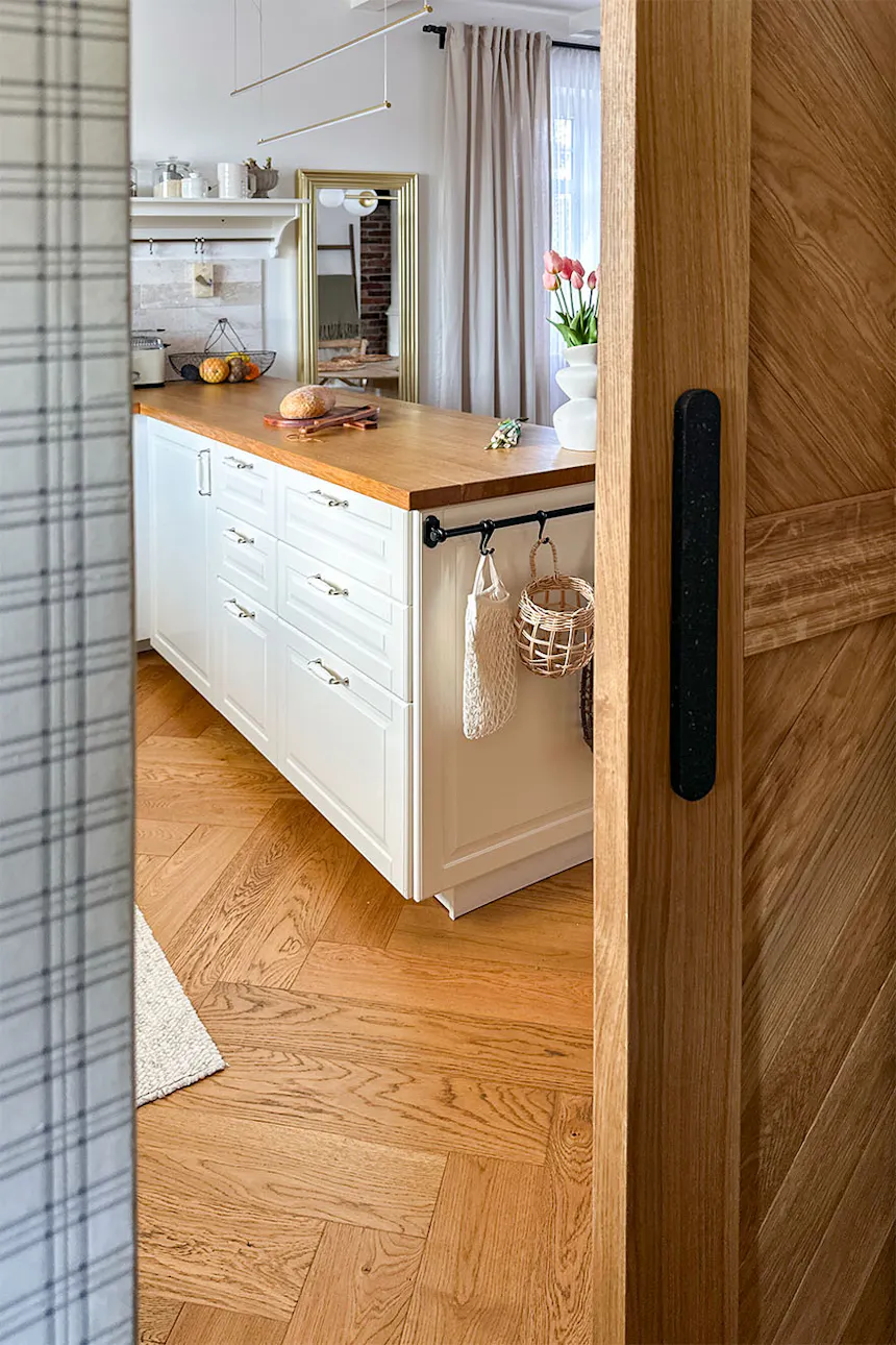 A view from the pantry onto a bright kitchen featuring an oak worktop and classic herringbone parquet flooring.