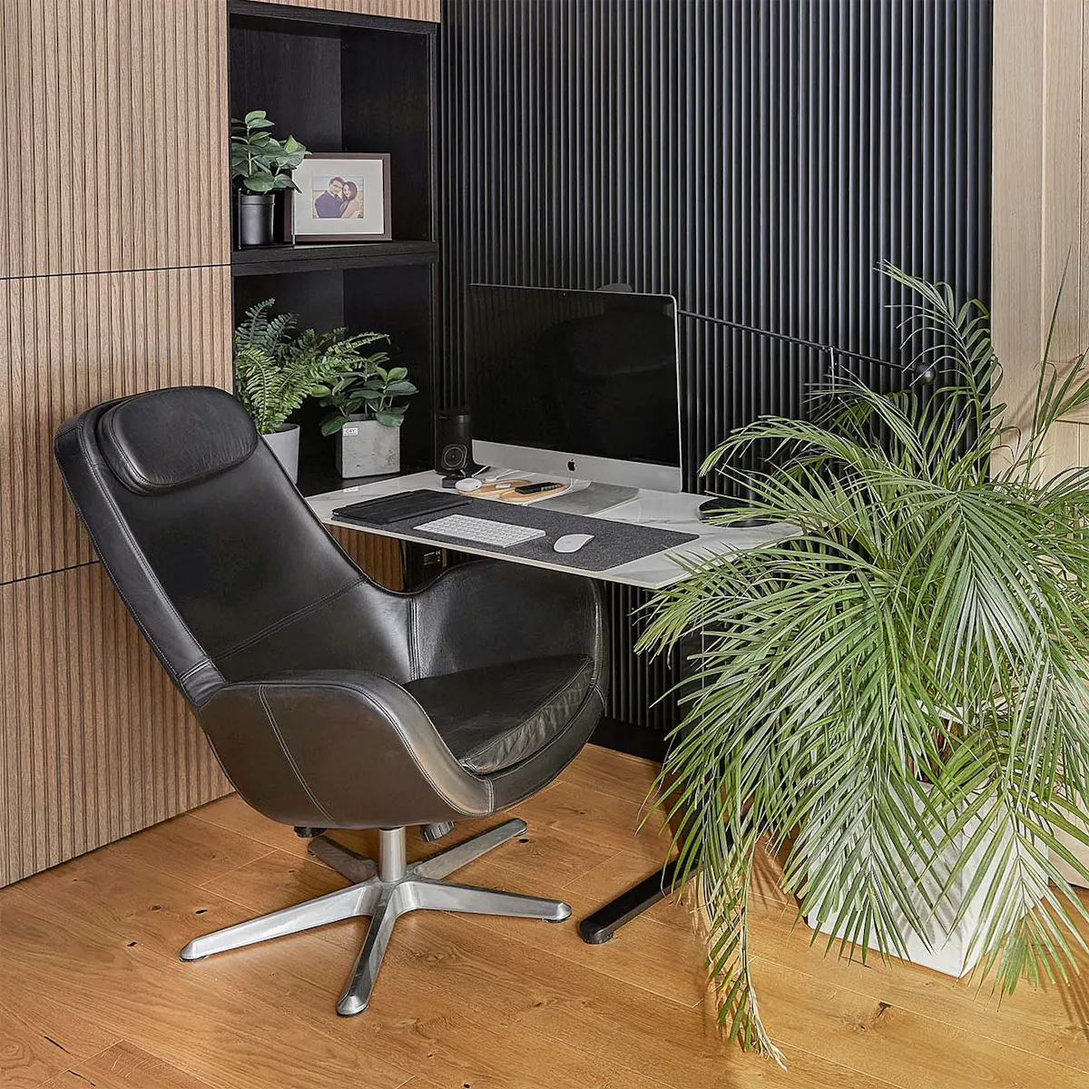 fauteuil en cuir noir, petit bureau, grande plante en pot et lattes murales noires dans le bureau à domicile