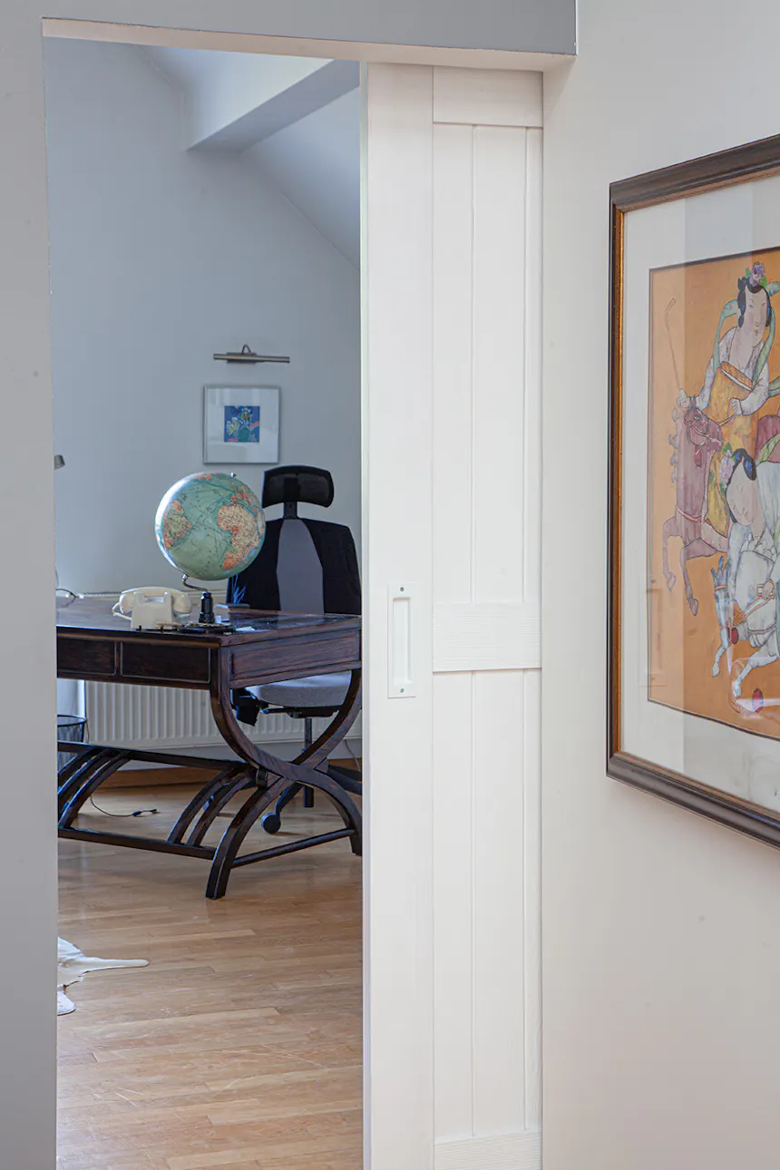 une porte blanche ouverte révélant une partie d'un bureau à domicile avec un bureau sombre