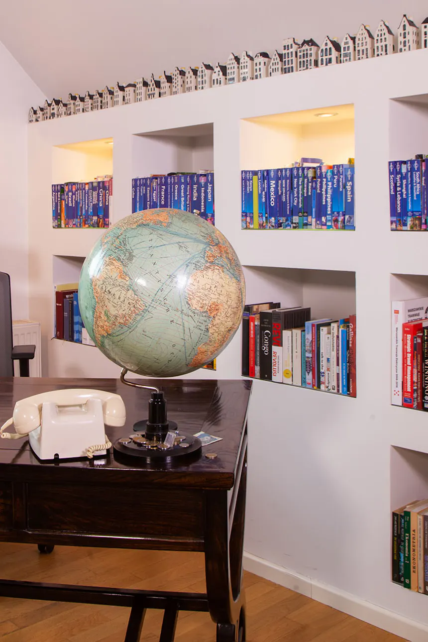un globe et un téléphone sur un bureau marron foncé contre un mur avec des étagères remplies de livres