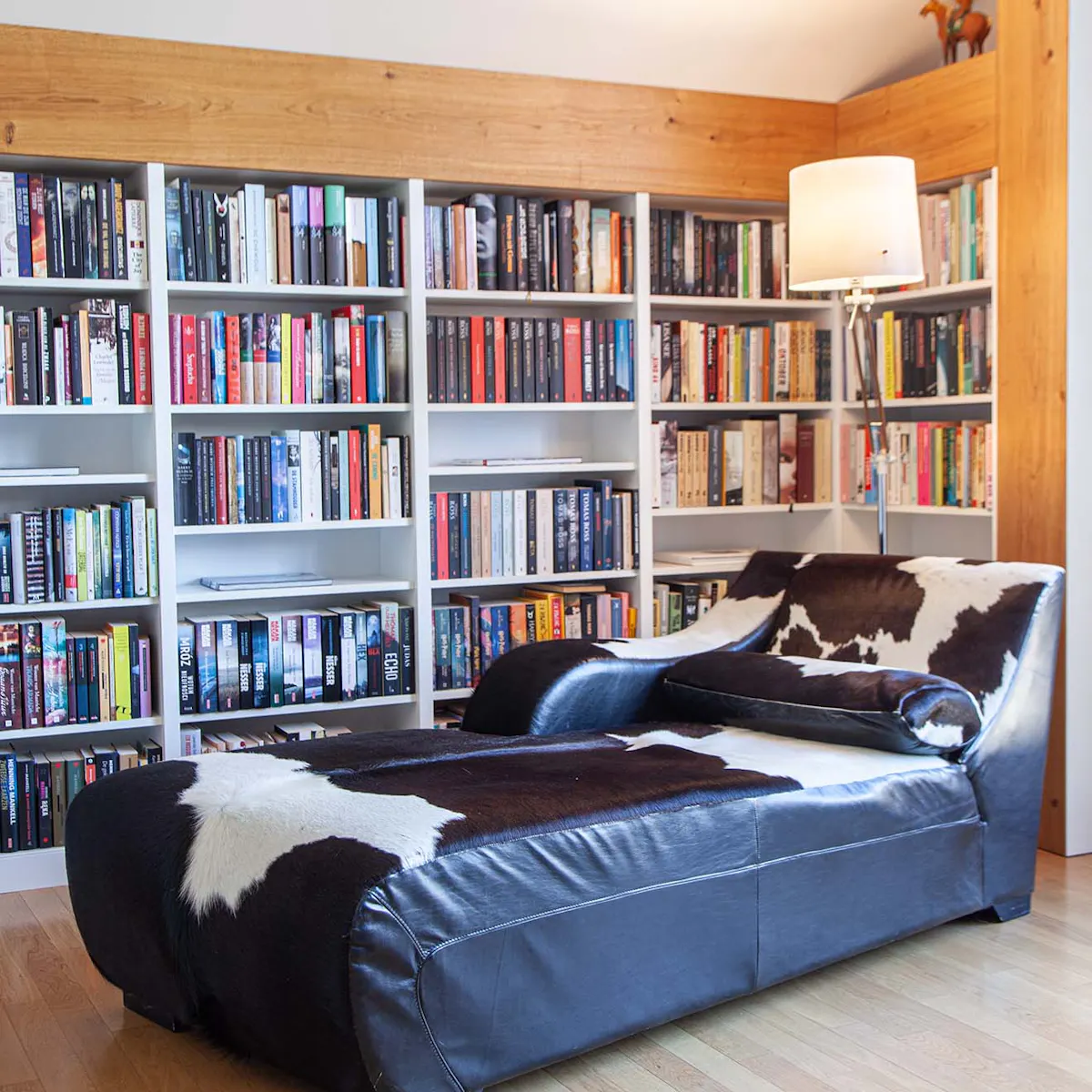une chaise longue avec un revêtement noir et blanc contre un mur rempli d'étagères avec des livres
