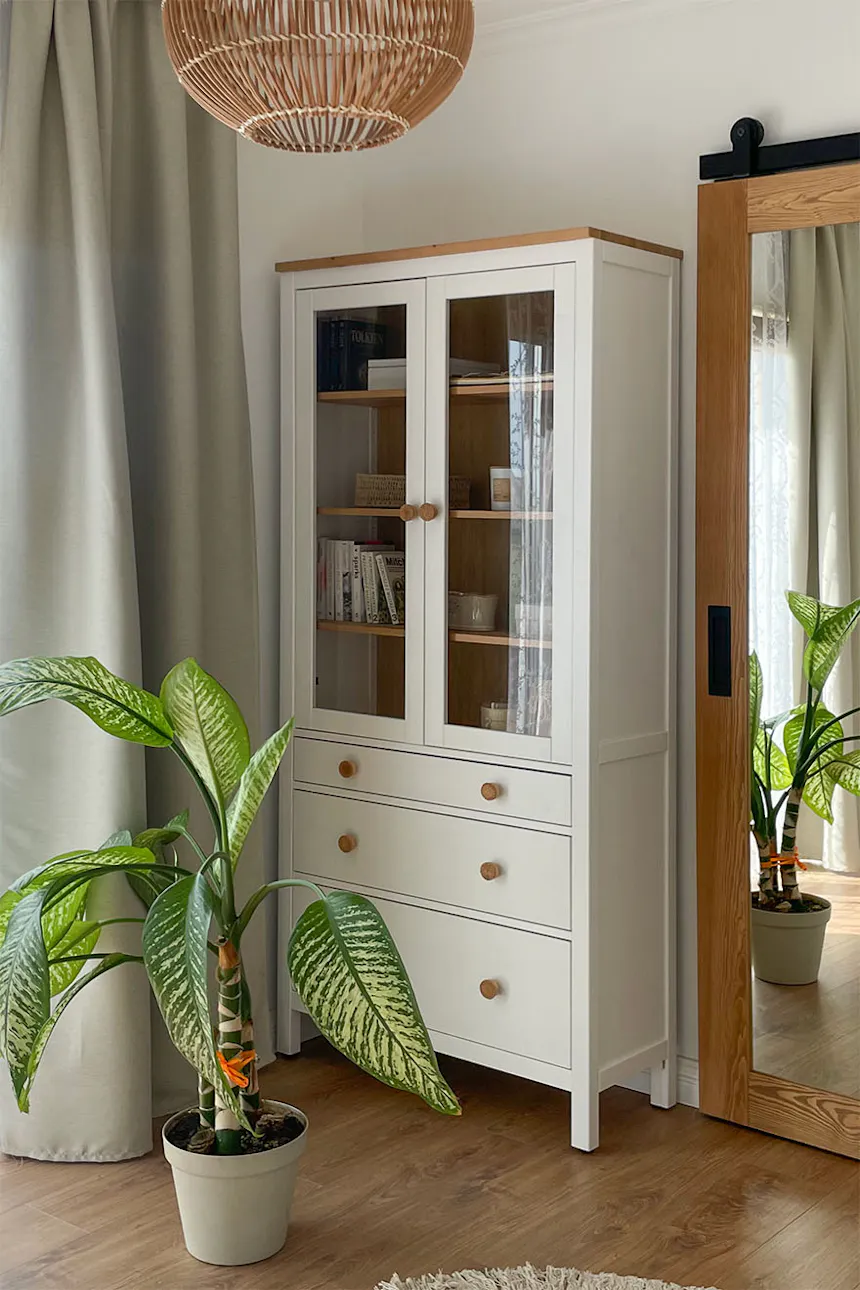 une vitrine blanche avec tiroirs et portes vitrées et une grande plante en pot dans la chambre