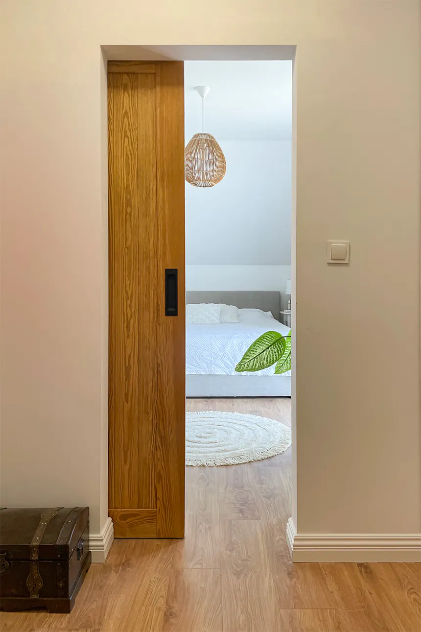 une porte coulissante ouverte révélant un fragment d'un grand lit dans la chambre