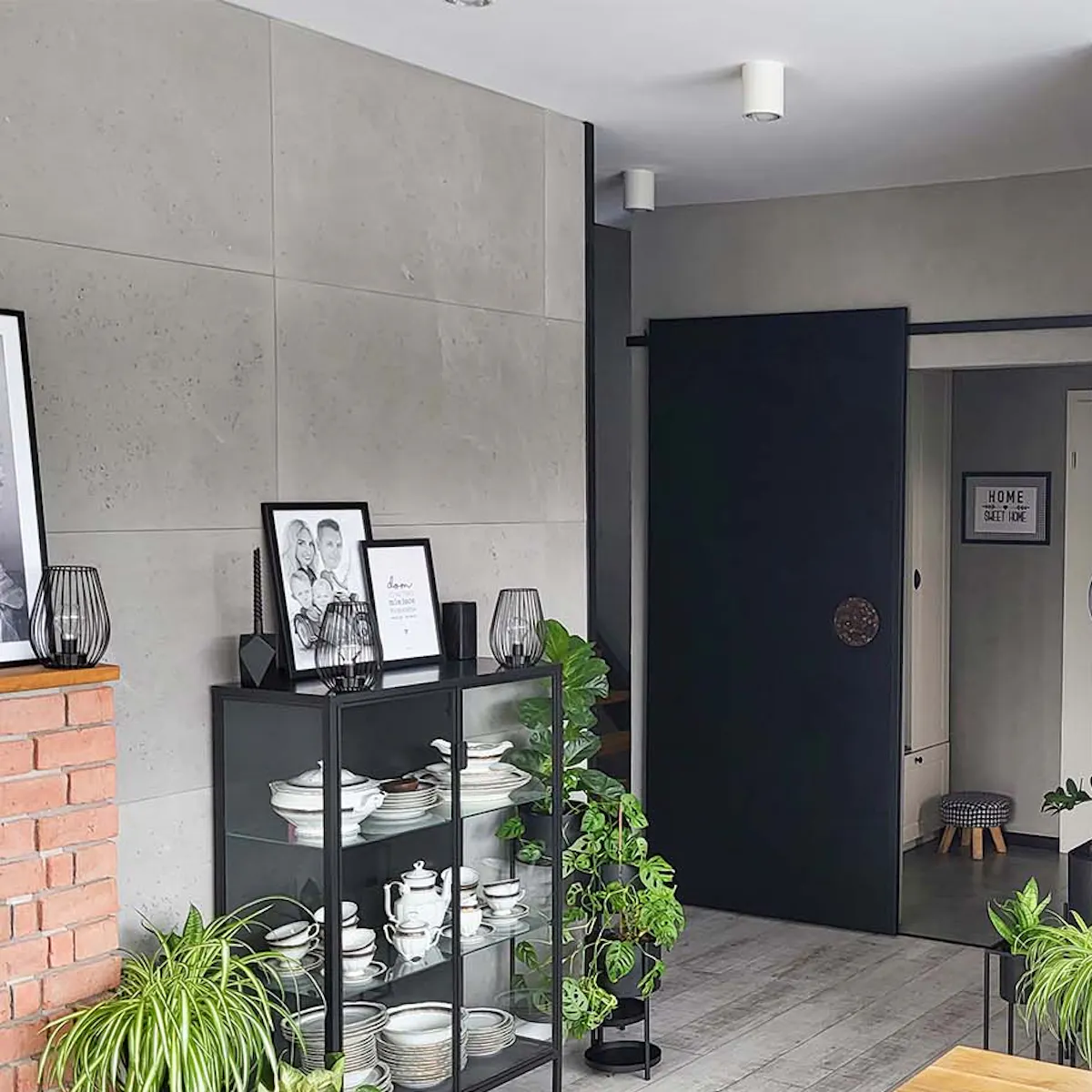 une table en bois sur pieds en métal, une vitrine en verre noir et des portes coulissantes noires dans un salon moderne